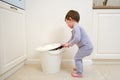 Toddler baby throws garbage in the trash can. A happy child lifts the lid