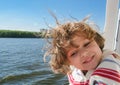 Toddler blonde smiling girl in a striped sweatshirt with her hair flying in the wind on a boat. Against the background of greenish Royalty Free Stock Photo