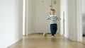 Toddler boy as he plays with a ball on the wooden floor of a long corridor in his house Royalty Free Stock Photo