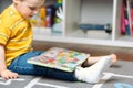 Toddler boy with a bandage or cast on his leg plays with colourful book. Fracture of a foot and finger in children Royalty Free Stock Photo