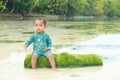 Toddler boy in blue swimsuit sitting on green trunk in shallow sea Royalty Free Stock Photo