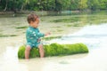 Toddler boy in blue swimsuit sitting and playing on green trunk in shallow sea Royalty Free Stock Photo