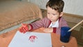 Toddler boy drawing with paints color with fingers on a table, sheets, hand and white wall background. School concept