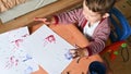 Toddler boy drawing with paints color with fingers on a table, sheets, hand and white wall background. School concept