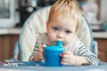 Toddler boy drinks from cup in high chair.