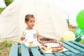 Toddler boy eating cheesecake with fruits and chocolate in front of tent Royalty Free Stock Photo