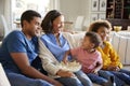 Toddler boy eating popcorn, sitting on the sofa with his sister and parents in their living room watching a movie together Royalty Free Stock Photo