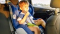 Little toddler boy feeling hungry and eating while travelling by car in child safety seat