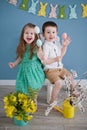 Toddler boy and girl play with easter decorations. Spring colorful decorations, bunny garland, flowers on blue background