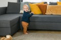 Toddler boy laughing having fun standing near sofa in living room at home copy space. Adorable baby making first steps Royalty Free Stock Photo