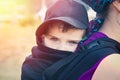 Toddler boy portrait in black cap in babycarrier on his mothers back