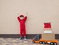 Toddler boy in a red overalls and a cap with a bright emotion of joy near a large toy car - truck with cardboard boxes Royalty Free Stock Photo