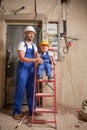 Man and child electricians posing near electrical panel in apartment.