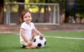 Toddler boy in sports uniform sitting with soccer ball at football field outdoors in summer day. Goalposts soccer nets in Royalty Free Stock Photo