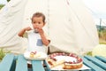 Toddler boy eating cheesecake with fruits and chocolate in front of tent Royalty Free Stock Photo