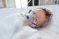 Toddler boy using nebulizer to cure asthma or pneumonia disease . Sick baby boy rest on patients bed and has inhalation therapy by Royalty Free Stock Photo