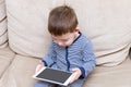 Toddler boy is using a tablet on a couch