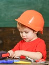 Toddler on busy face plays with bolts at home in workshop. Kid boy play as handyman. Child in hard hat, helmet playing