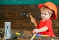 Toddler on busy face plays with hammer tool at home in workshop. Child in helmet cute playing as builder or repairer