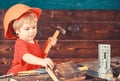 Toddler on busy face plays with hammer tool at home in workshop. Child in helmet cute playing as builder or repairer Royalty Free Stock Photo