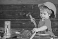 Toddler on busy face plays with hammer tool at home in workshop. Child in helmet cute playing as builder or repairer Royalty Free Stock Photo