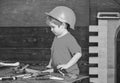 Toddler on busy face plays at workshop near table with tools. Workshop and tools concept. Kid boy playing with