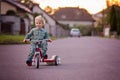 Toddler child, blond boy, riding tricycle in a village small road on sunset