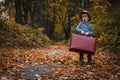 Toddler child boy in a hat and retro style holds an old suitcase against the backdrop of an autumn park and dry leaves Royalty Free Stock Photo