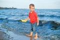 toddler child boy putting yellow paper boat in water on lake sea ocean shore Royalty Free Stock Photo