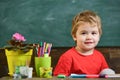 Toddler cute and cheerful ready to study. Kid boy in classroom near flower in pot and pencils, chalkboard on background Royalty Free Stock Photo