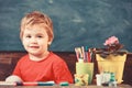 Toddler cute and cheerful ready to study. Kid boy in classroom near flower in pot and pencils, chalkboard on background Royalty Free Stock Photo