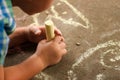 Toddler drawing withcolorful chalk against concrete outdoor.