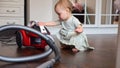 Toddler girl brings vacuum cleaner to tidy up spacious room