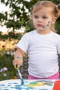 Toddler girl drawing with paint and brush. outdoors in garden, at home in backyard. vertical photo. Royalty Free Stock Photo