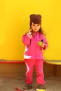 Toddler girl drinking `coffee` in sand box against sunlit bright yellow backdrop