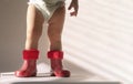 Toddler girl feet in red polka dot rubber boots in the shade in the sun. Little fashionista in boots and a diaper. No face