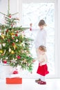 Toddler girl helping her brother to decorate Christmas tree