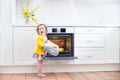 Toddler girl in kitchen mittens next to oven with apple pie