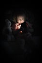 Toddler girl lying on bed with stuffed animal and playing with smarthphone at night