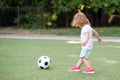 Toddler girl in pink sneakers playing football at stadium. Little blonde child preparing to kick soccer ball outdoors Royalty Free Stock Photo