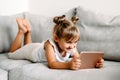 Toddler girl playing with digital wireless tablet computer on couch at home. Baby child growing with online applications. Child