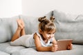 Toddler girl playing with digital wireless tablet computer on couch at home.