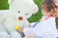 Toddler girl playing doctor with teddy bear putdoors