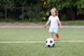 Toddler girl playing football: blonde child running on stadium to kick soccer ball. Outdoors activity and sports games concept Royalty Free Stock Photo
