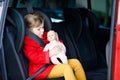 Toddler girl sitting in car seat, holding favourite doll toy and looking out of the window on nature and traffic. Little kid Royalty Free Stock Photo