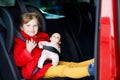 Toddler girl sitting in car seat, holding favourite doll toy and looking out of the window on nature and traffic. Little Royalty Free Stock Photo