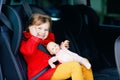 Toddler girl sitting in car seat, holding favourite doll toy and looking out of the window on nature and traffic. Little Royalty Free Stock Photo