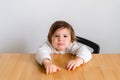 Toddler girl unhappy sitting at wooden desk. Tired child, hungry kid