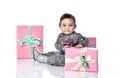 Toddler in gray suit and boots. She smiling, posing with pink decorated gift boxes, sitting on floor isolated on white. Close up Royalty Free Stock Photo