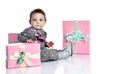 Toddler in gray suit and boots. She smiling, posing with pink decorated gift boxes, sitting on floor isolated on white. Close up Royalty Free Stock Photo